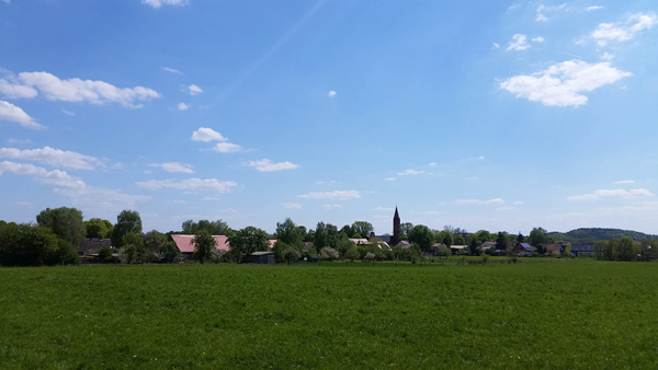 kleines Dorf mit Kirche hinter einem Feld am Radweg Eberswalde nach Prenzlau